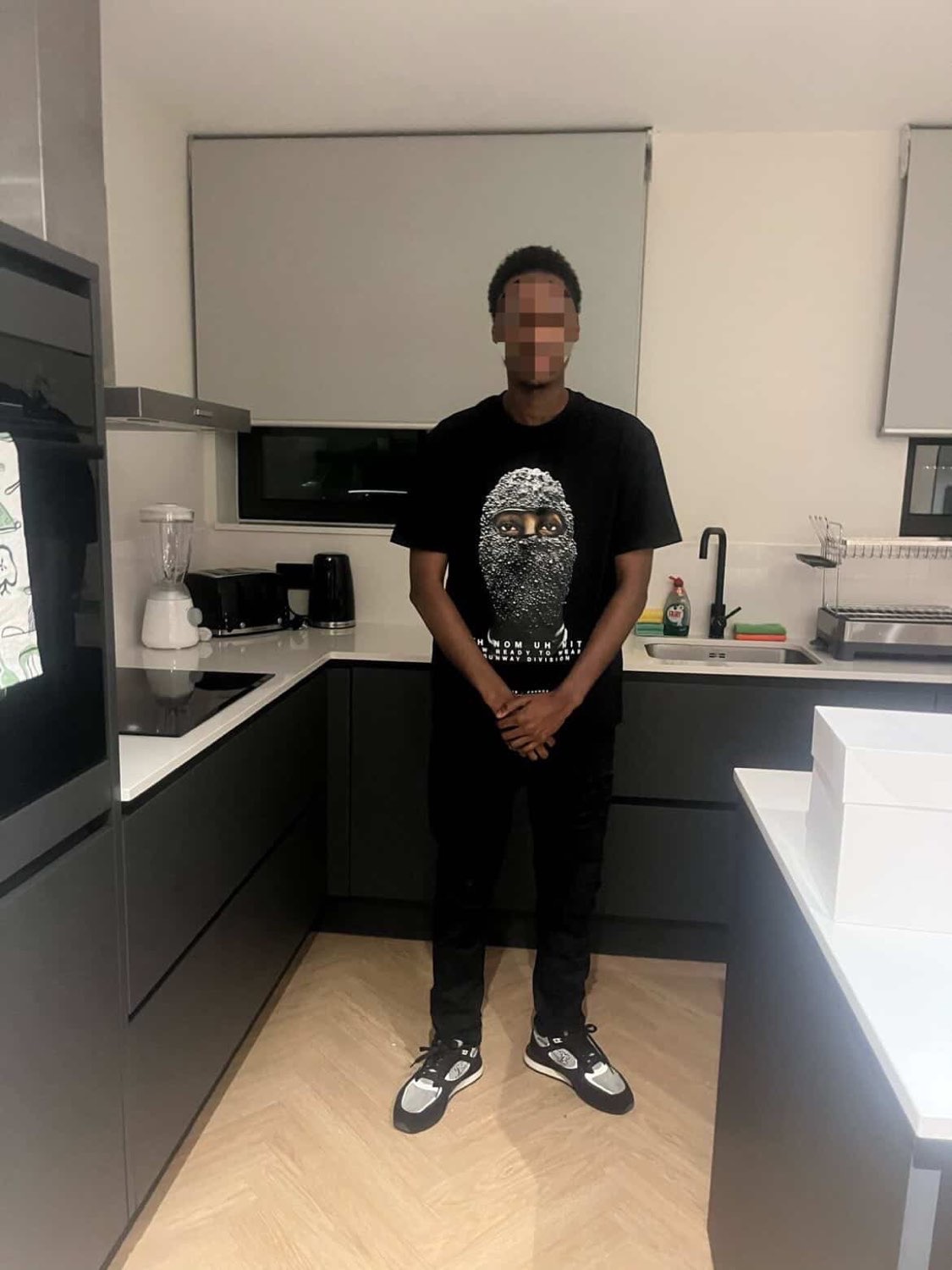 Client standing in a kitchen in a black graphic tee and trainers